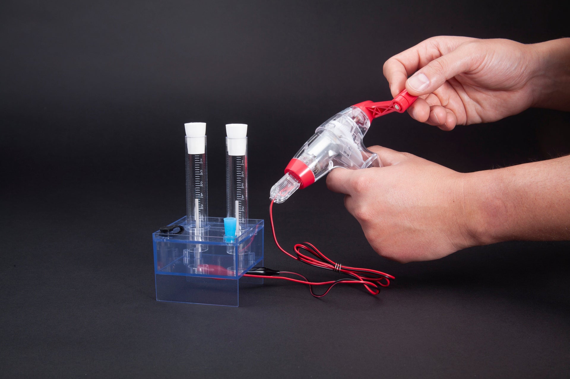 Person holding a Genecon hand crank generator connected to an electrolysis apparatus performing an electrochemistry experiment
