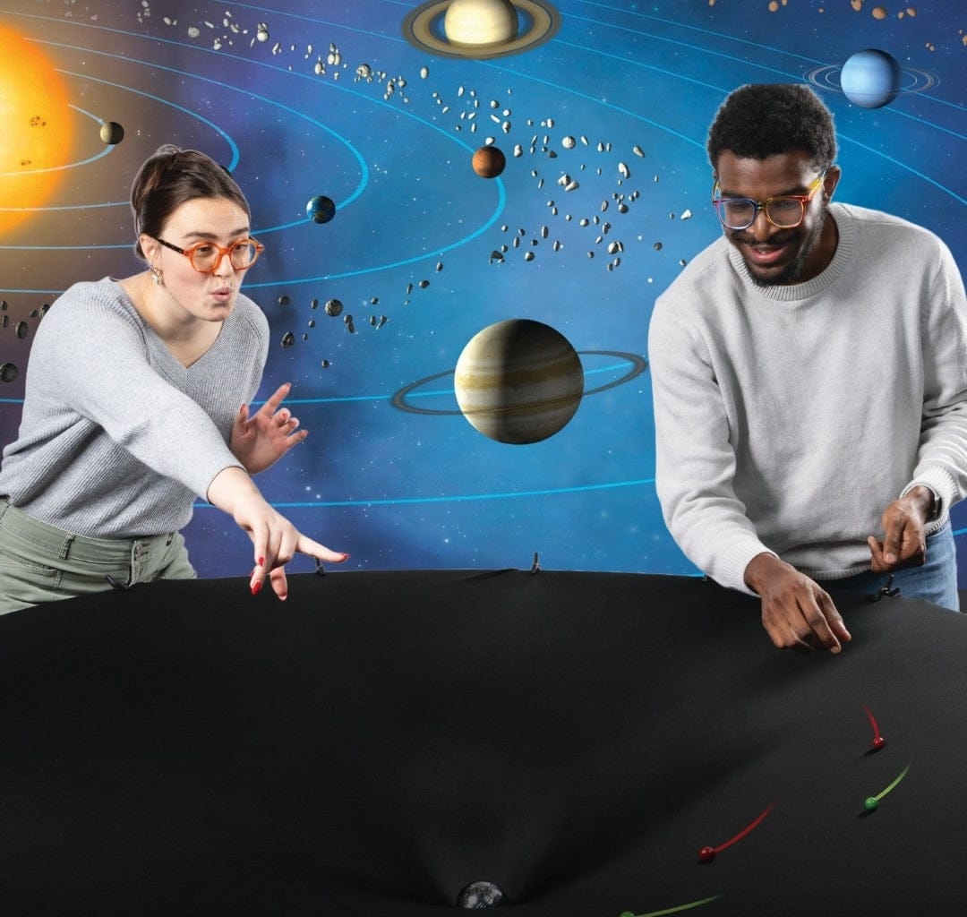 Two students playing with a Gravity Well on a background of a diagram of the solar system
