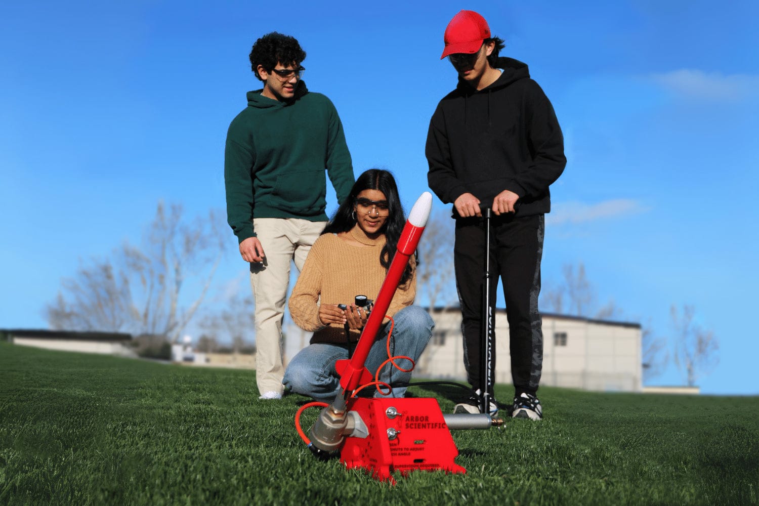 Three students with an Arbor Scientific air-powered rocket used to study projectile motion in physics.